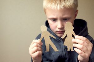 a blond boy with a sad face plays with paper dolls of a father and mother